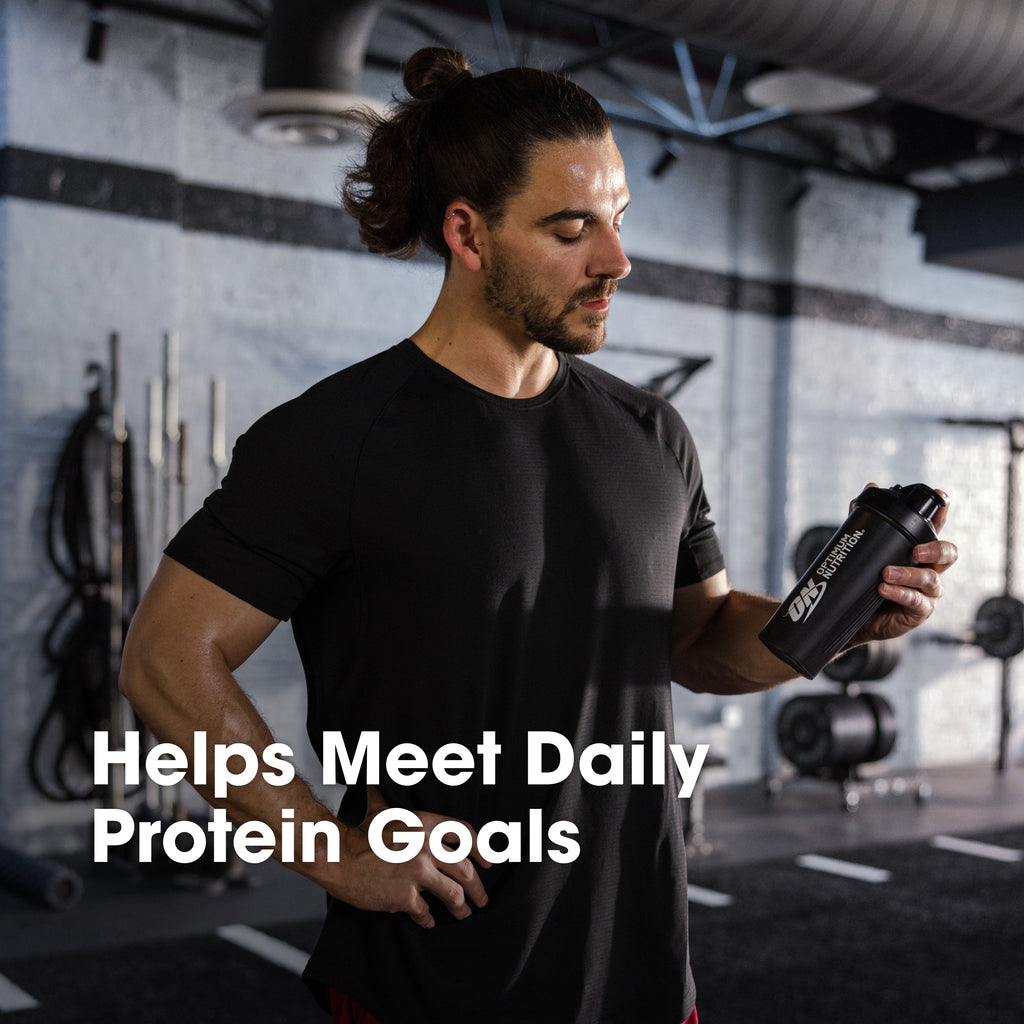 Man in a gym holding a protein shaker with text 'Helps Meet Daily Protein Goals'.